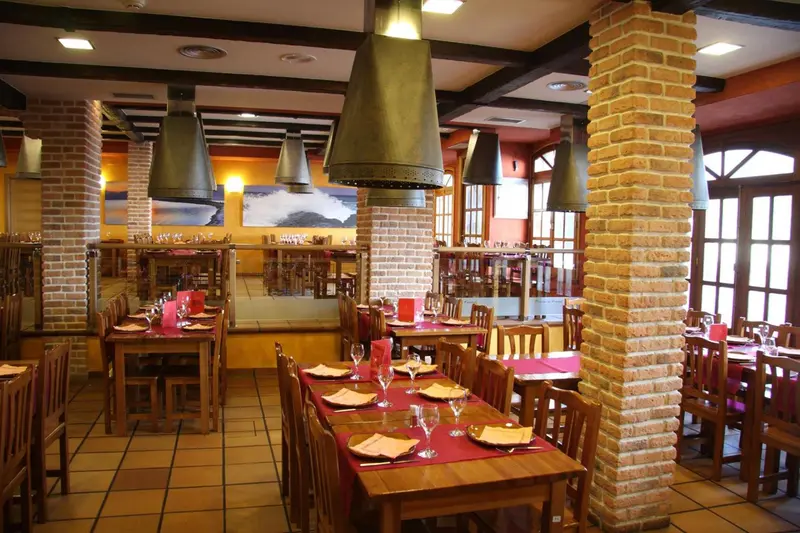 Une salle de restaurant avec des tables dressées et des suspensions métalliques.