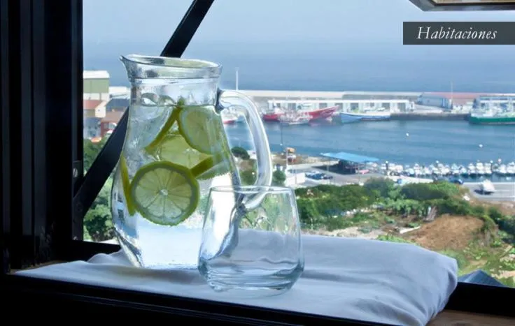 Une carafe d'eau fraîche avec des tranches de citron et un verre sur une table en lin, avec vue sur un port de plaisance.