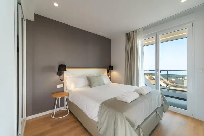 Une chambre lumineuse avec un grand lit et un accès à un balcon.