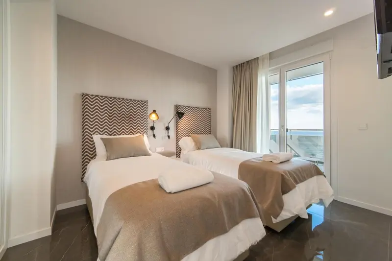 Une chambre lumineuse avec deux lits simples et une porte-fenêtre donnant sur l'extérieur.