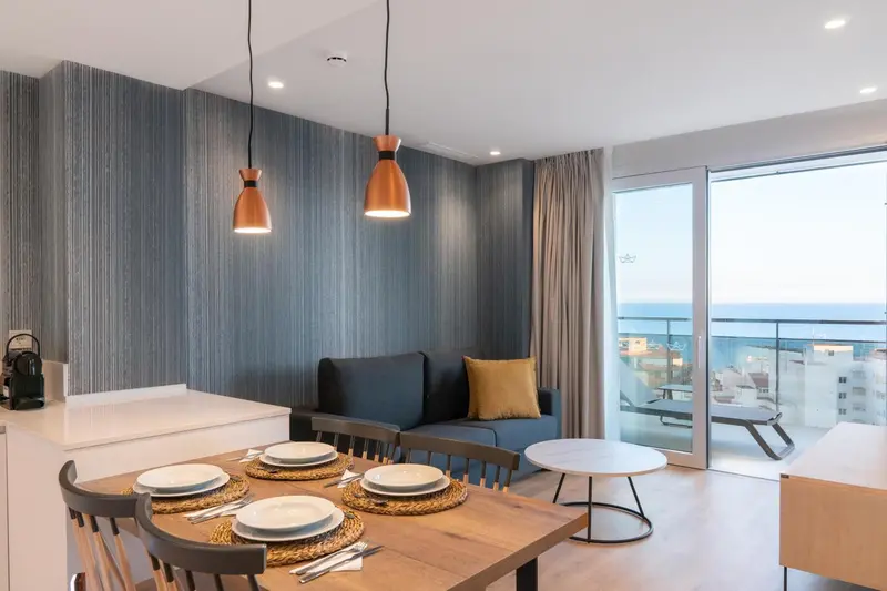 Un espace de vie lumineux avec un coin repas et un canapé face à une baie vitrée.