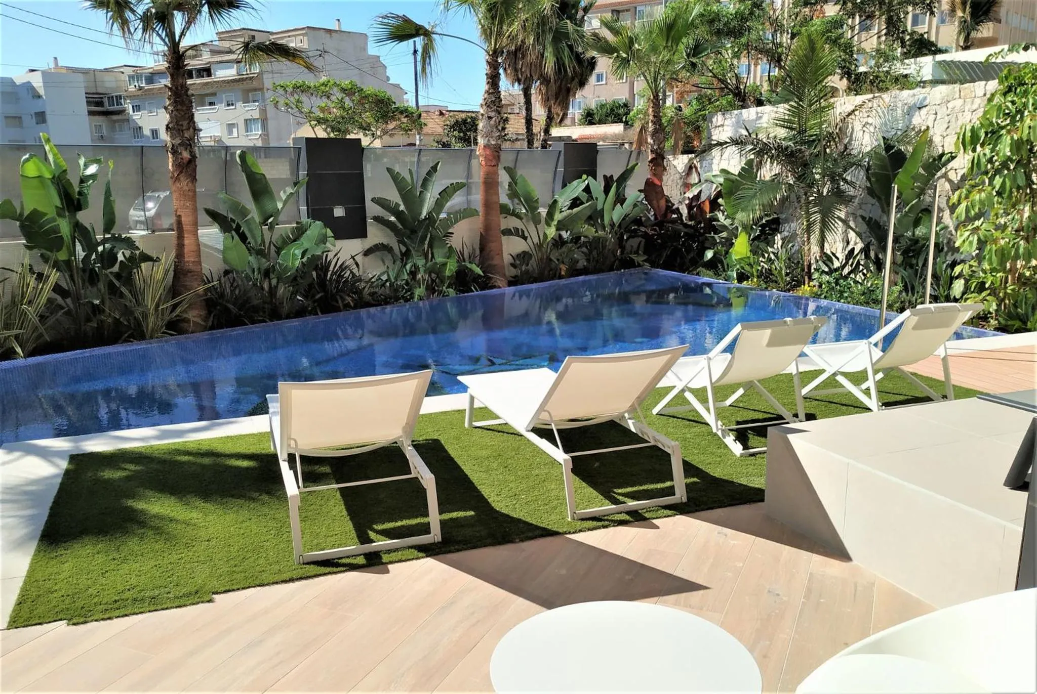 Transats blancs disposés autour d'une piscine rectangulaire dans un jardin tropical.