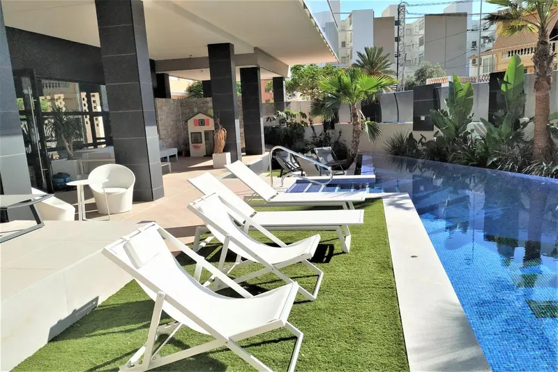 Transats blancs disposés au bord d'une piscine rectangulaire.