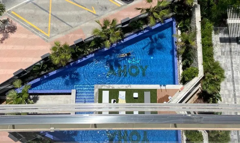 Vue aérienne d'une piscine rectangulaire entourée de végétation et de terrasses.