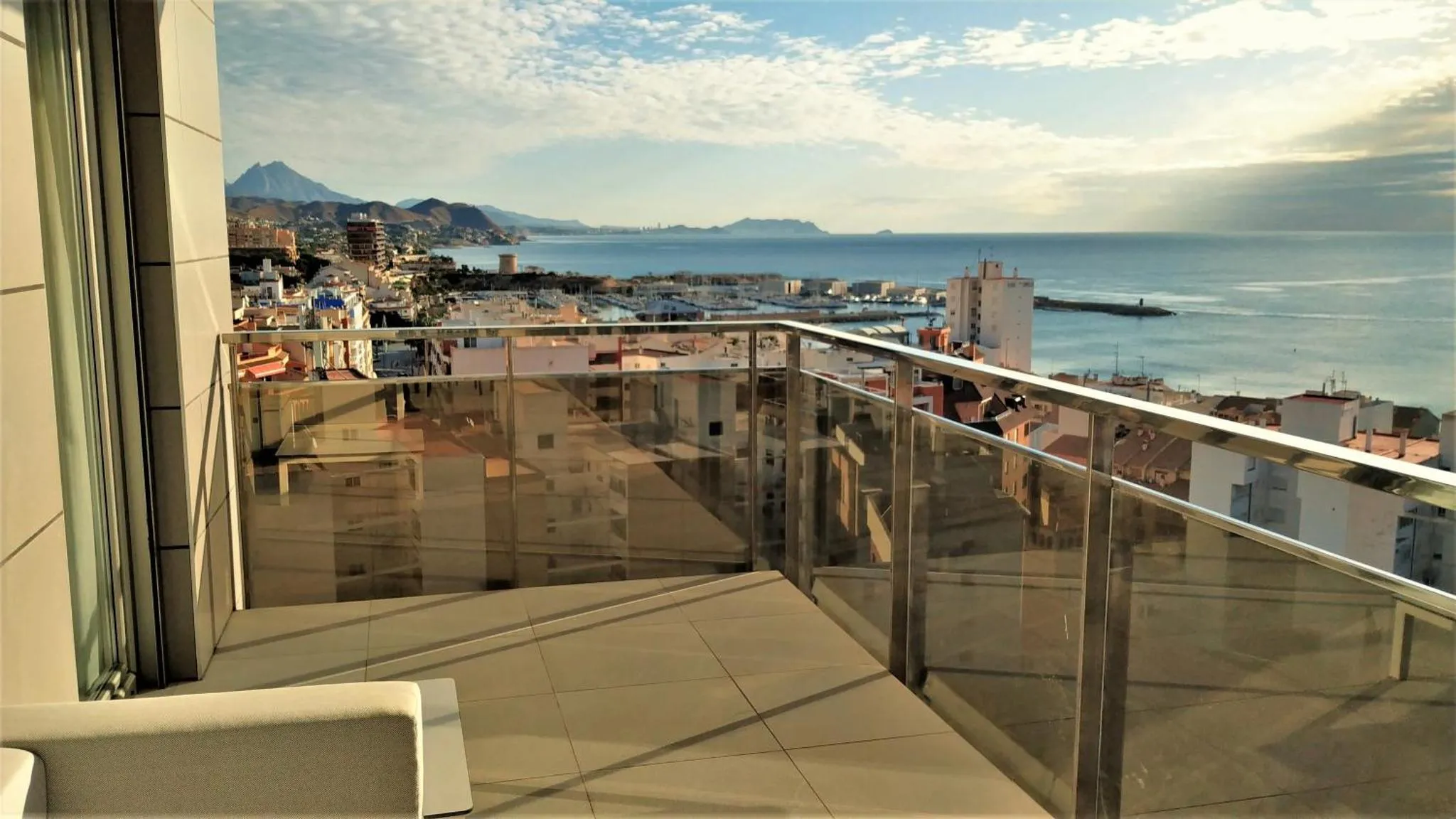 Vue d'une terrasse avec une rambarde en verre donnant sur la mer et les montagnes.