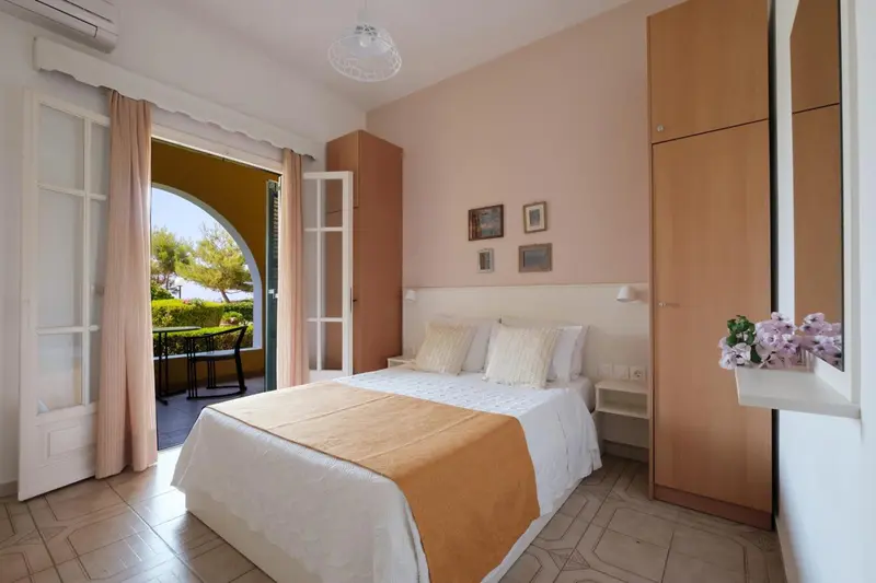 Chambre lumineuse avec un lit recouvert d'une courtepointe et une porte ouverte sur une terrasse.