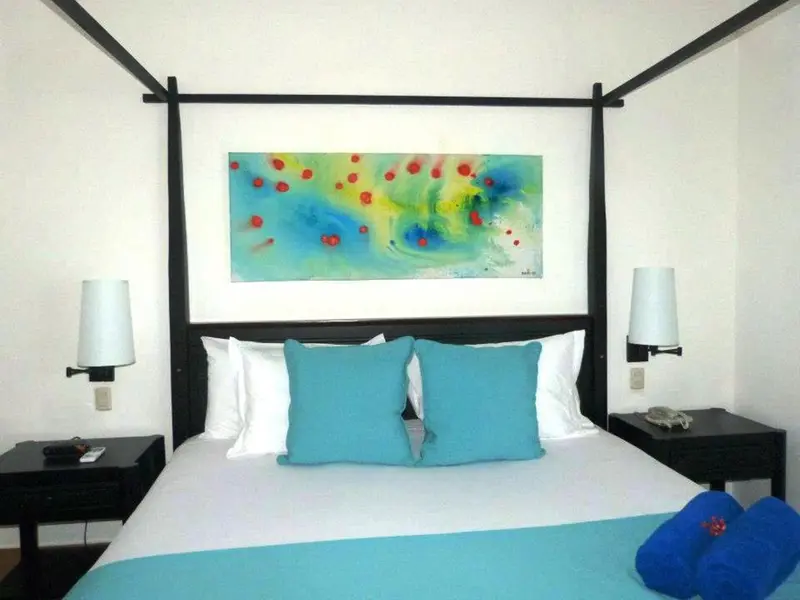 Une chambre lumineuse avec un grand lit recouvert d'une courtepointe turquoise et de coussins bleus.