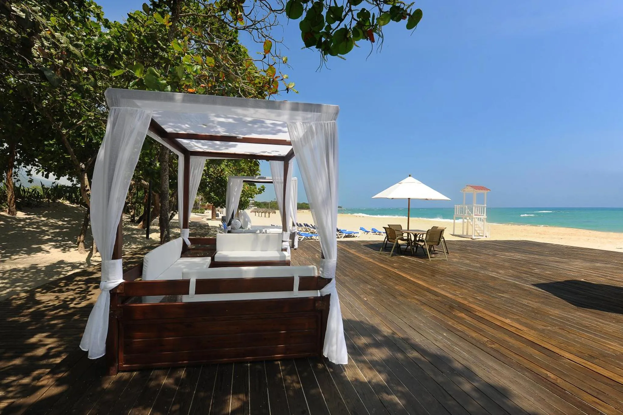 Un espace de détente ombragé sur une terrasse en bois face à la mer.