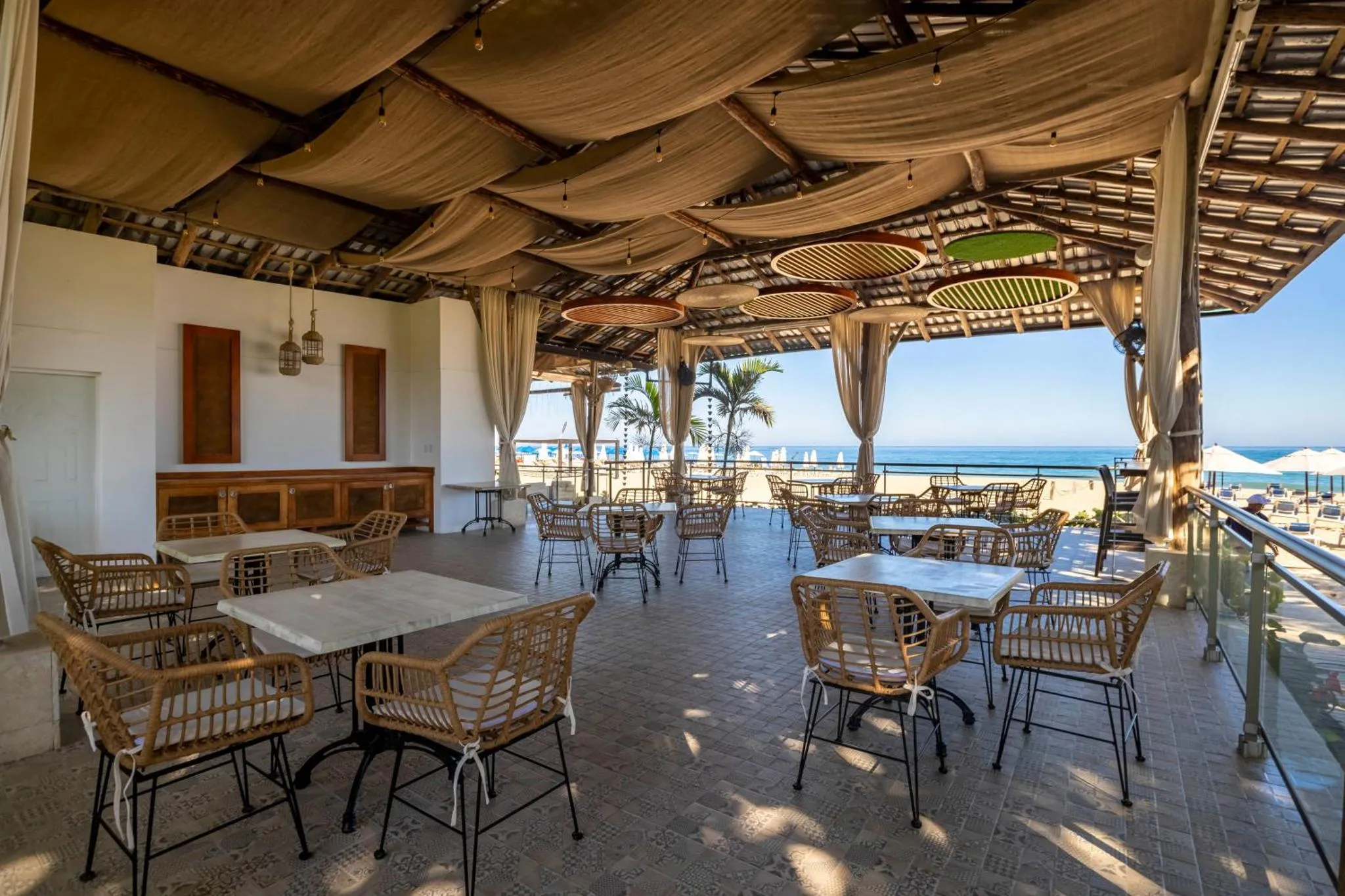 Terrasse ombragée avec tables et chaises donnant sur la mer.