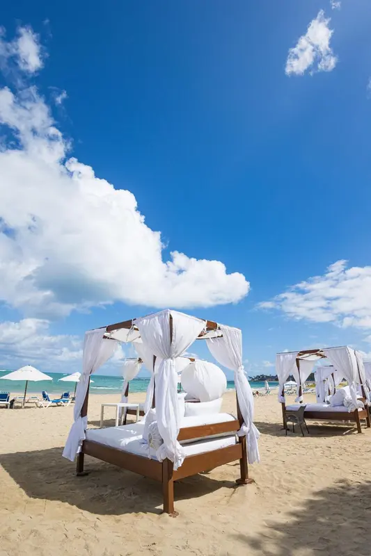 Transats blancs sous des structures en bois sur une plage de sable fin.