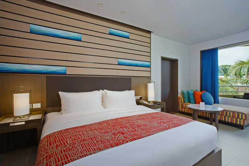 Une chambre lumineuse avec un grand lit et un coin salon près de la fenêtre.