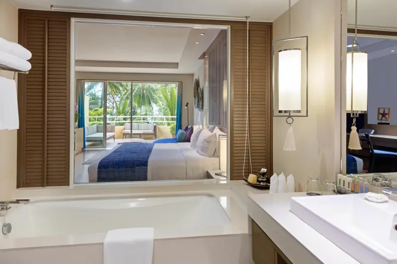 Une baignoire blanche est visible au premier plan, avec une chambre à coucher et un balcon en arrière-plan.