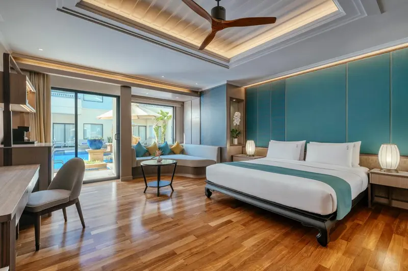 Une chambre spacieuse avec un lit et un coin salon donnant sur une piscine.
