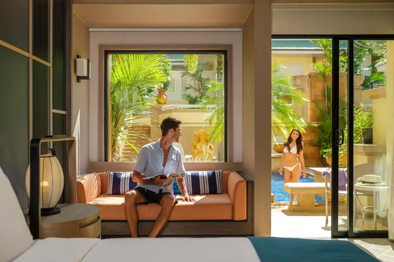 Un couple se détend dans un espace de vie lumineux donnant sur une piscine et une végétation luxuriante.