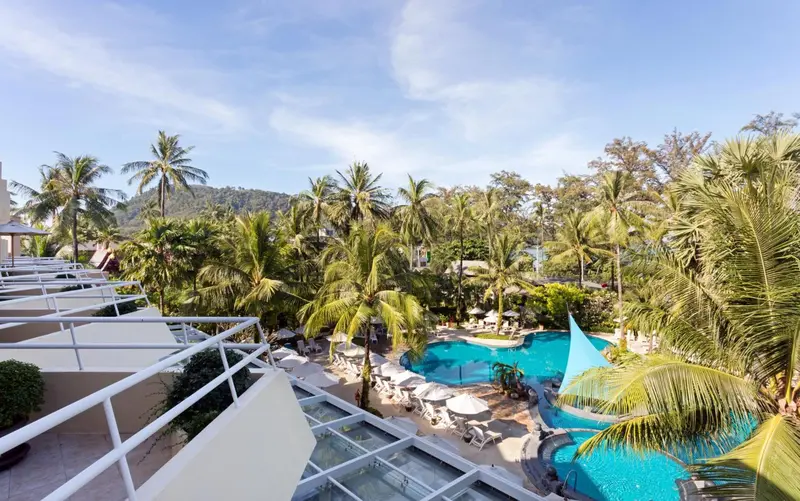 Vue aérienne sur une piscine turquoise entourée de végétation luxuriante et de bâtiments.