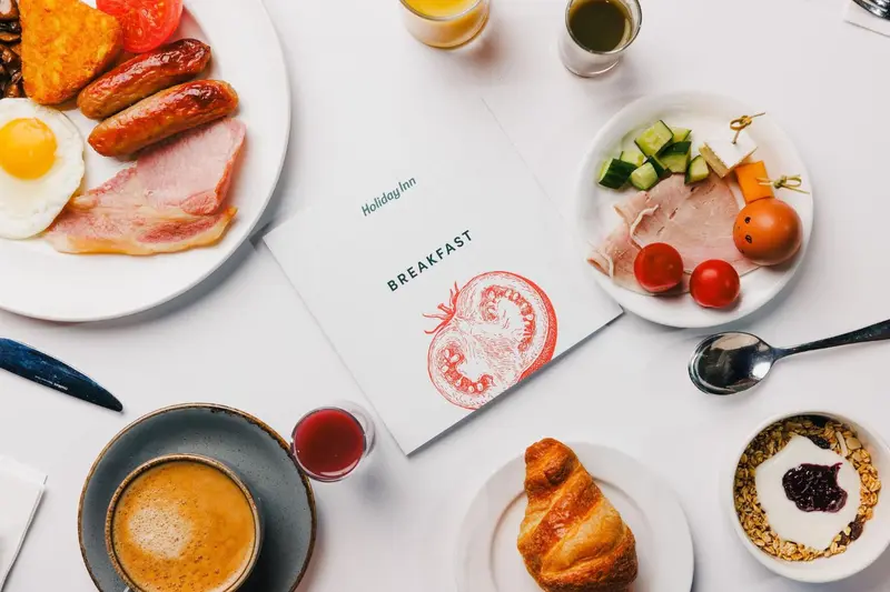 Une table blanche présente un petit-déjeuner copieux avec des œufs, du bacon, des saucisses et des fruits.