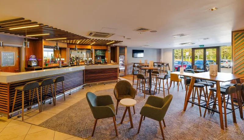Un bar spacieux avec un comptoir en bois et des tables hautes.