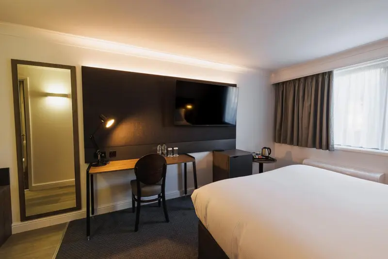 Une chambre d'hôtel moderne avec un lit, un bureau et une télévision murale.