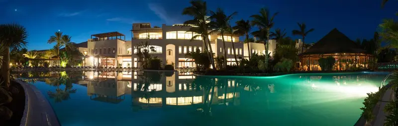 Bâtiment éclairé au bord d'une piscine la nuit.