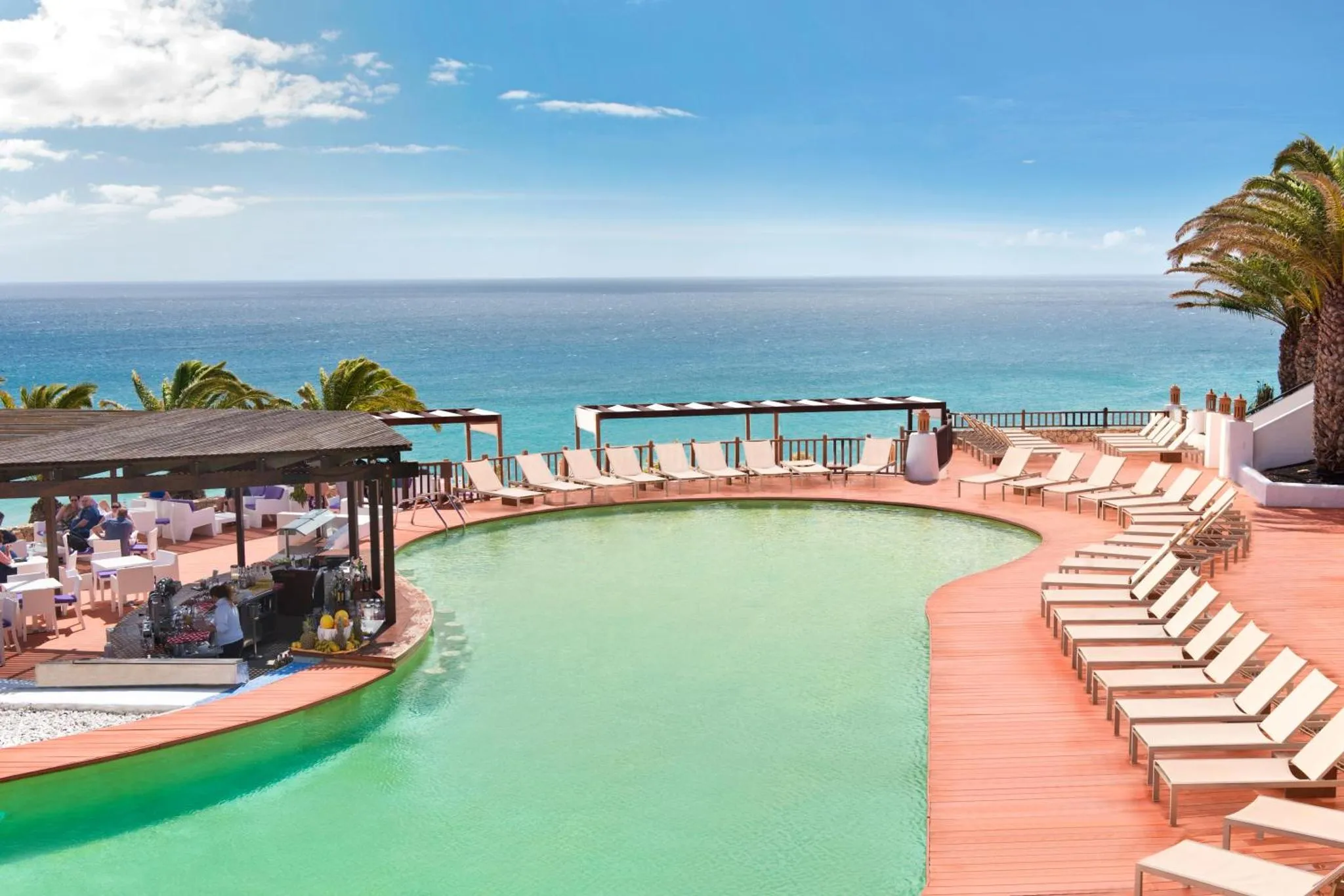 Une piscine avec des transats et un bar en bord de mer.