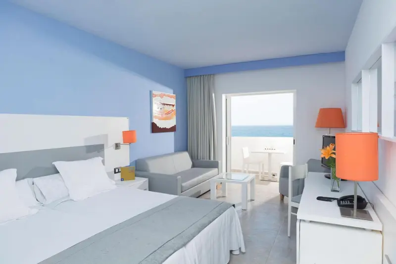 Chambre lumineuse avec un lit double et un canapé face à une baie vitrée.