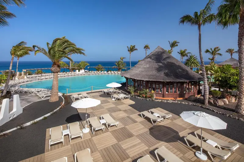 Terrasse avec transats et parasols donnant sur une piscine et la mer.