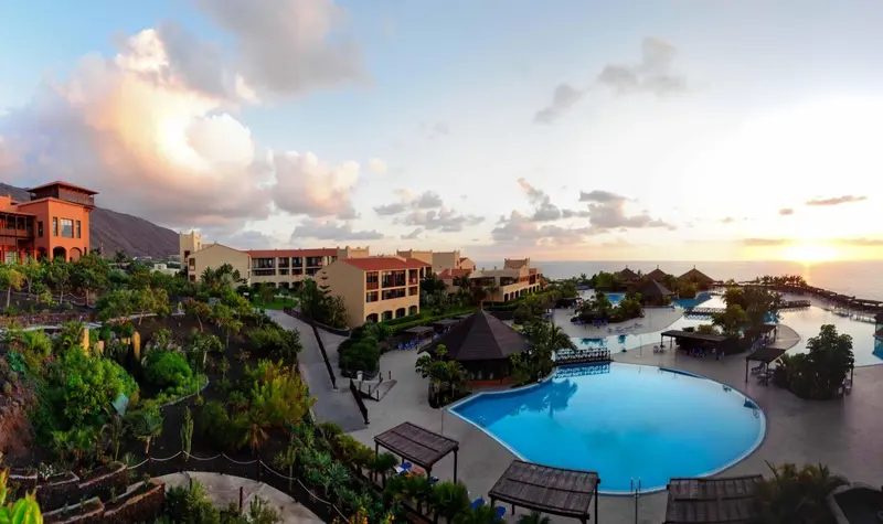 Vue aérienne d'un complexe hôtelier avec piscine et végétation luxuriante au coucher du soleil.