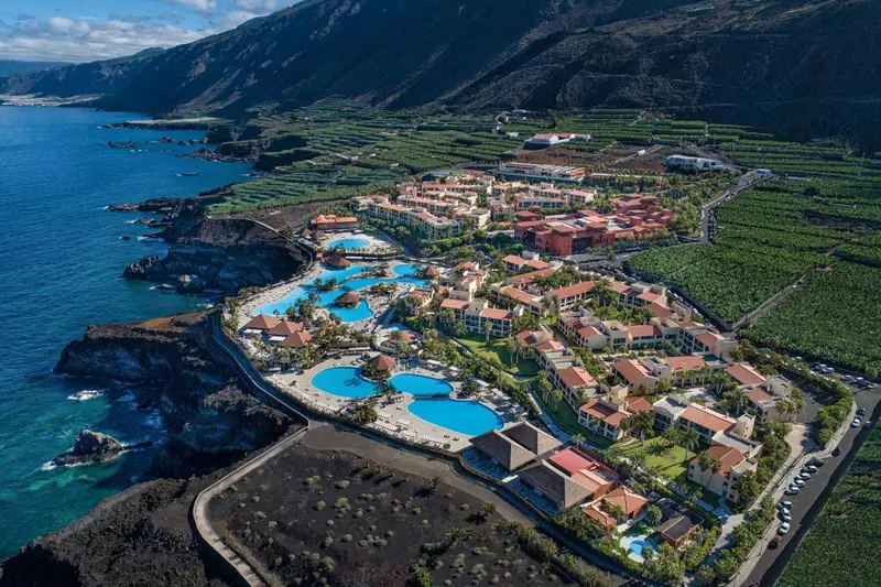 Vue aérienne d'un complexe hôtelier avec piscines et végétation luxuriante au bord de l'océan.