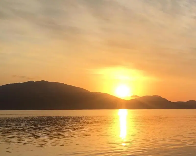Coucher de soleil sur une mer calme avec des montagnes en arrière-plan.