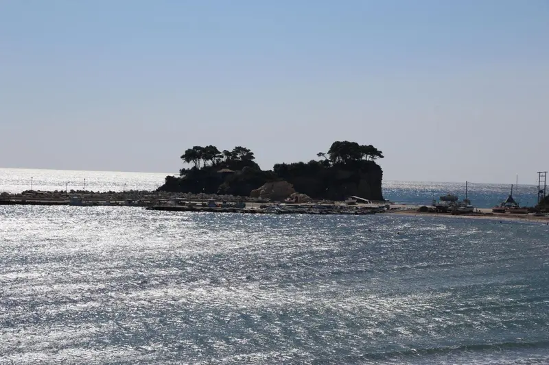 Vue d'une île rocheuse couverte de végétation au large d'une plage ensoleillée.