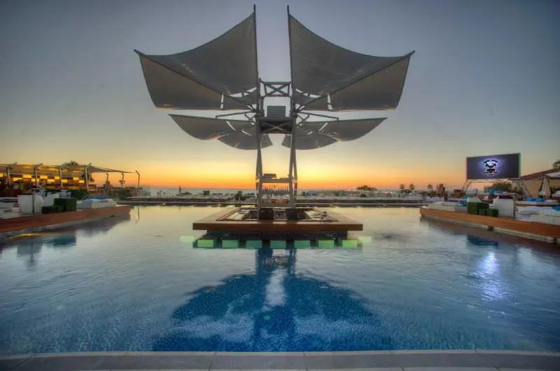 Une piscine rectangulaire avec une structure architecturale au centre et un coucher de soleil en arrière-plan.