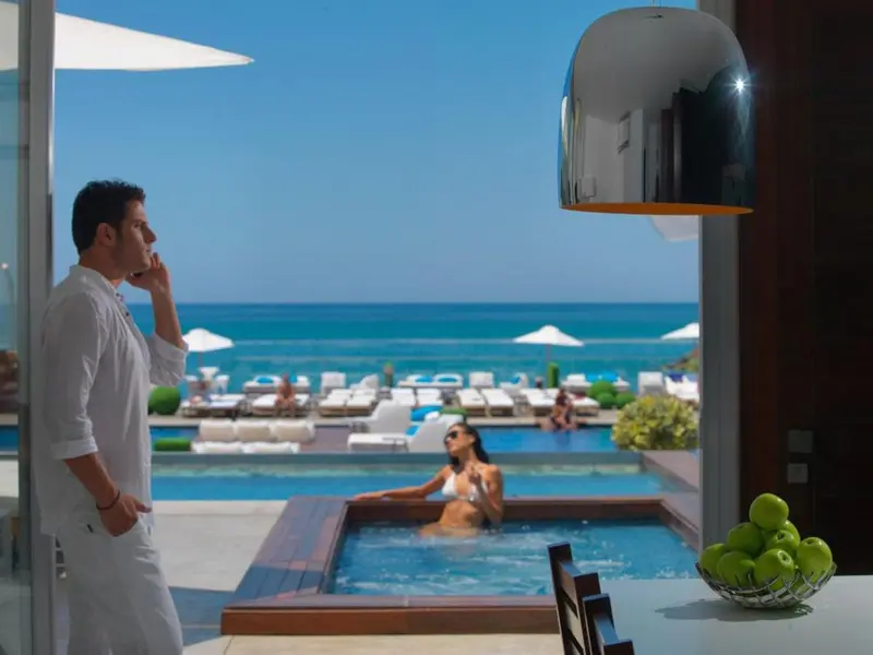Un homme parle au téléphone face à une piscine et à la mer.