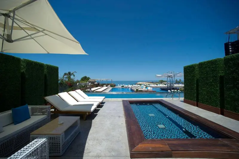 Transats blancs disposés autour d'une piscine bleue et d'un jacuzzi, avec vue sur un port de plaisance.