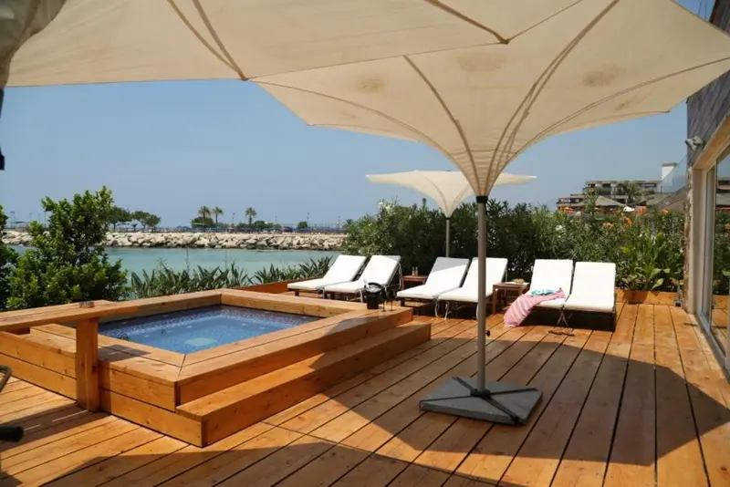 Terrasse en bois avec jacuzzi et chaises longues face à la mer.