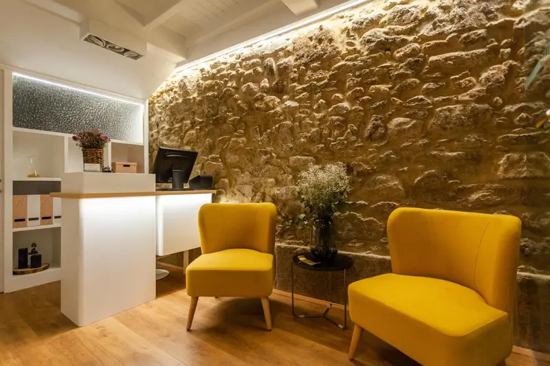 Un comptoir d'accueil moderne est flanqué de deux fauteuils jaunes devant un mur en pierre.