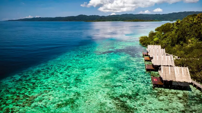 Cabanes sur pilotis au-dessus d'un lagon turquoise et d'un récif corallien.