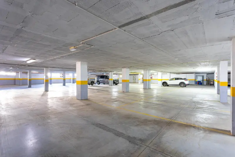Vaste parking souterrain avec des voitures stationnées et des piliers peints.