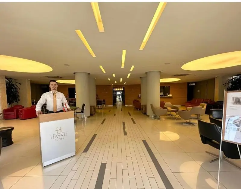 Un employé d'accueil se tient devant un comptoir dans un hall d'hôtel lumineux.