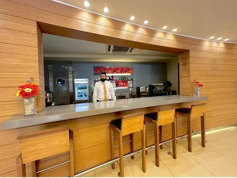 Un comptoir de bar en bois clair avec un employé et des tabourets hauts.
