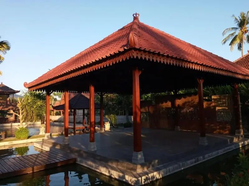 Pavillon ouvert en bois avec toiture rouge et vue sur une piscine et la végétation.