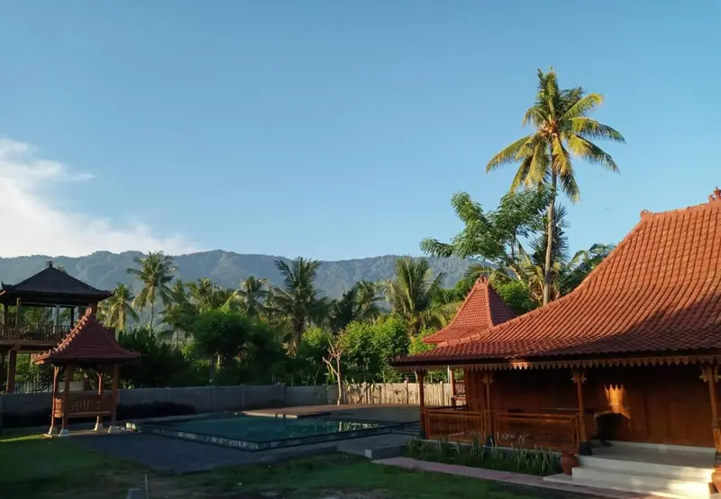 Bâtiments traditionnels avec toits rouges et végétation luxuriante devant une piscine.