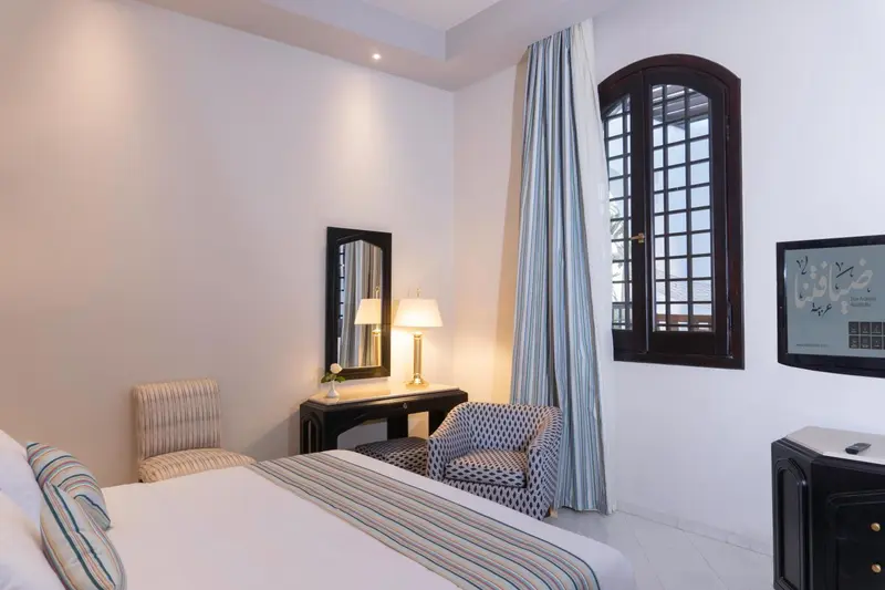 Une chambre lumineuse avec un lit, un bureau et deux fauteuils.