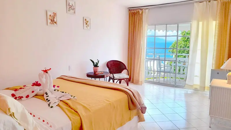 Une chambre lumineuse avec un lit decoré de serviettes en forme de cygnes et une vue sur la mer.
