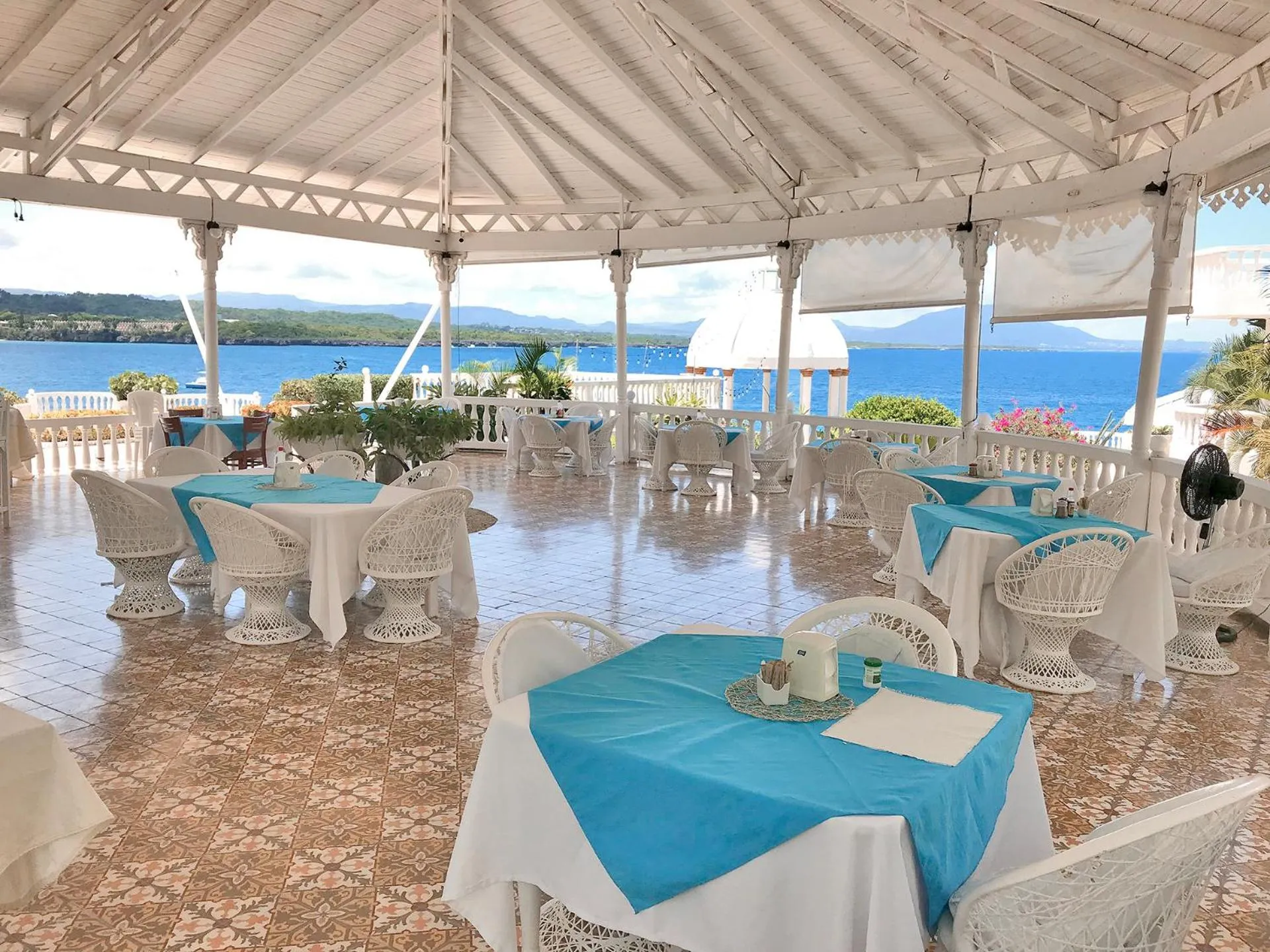 Terrasse ombragée avec tables et chaises donnant sur la mer.