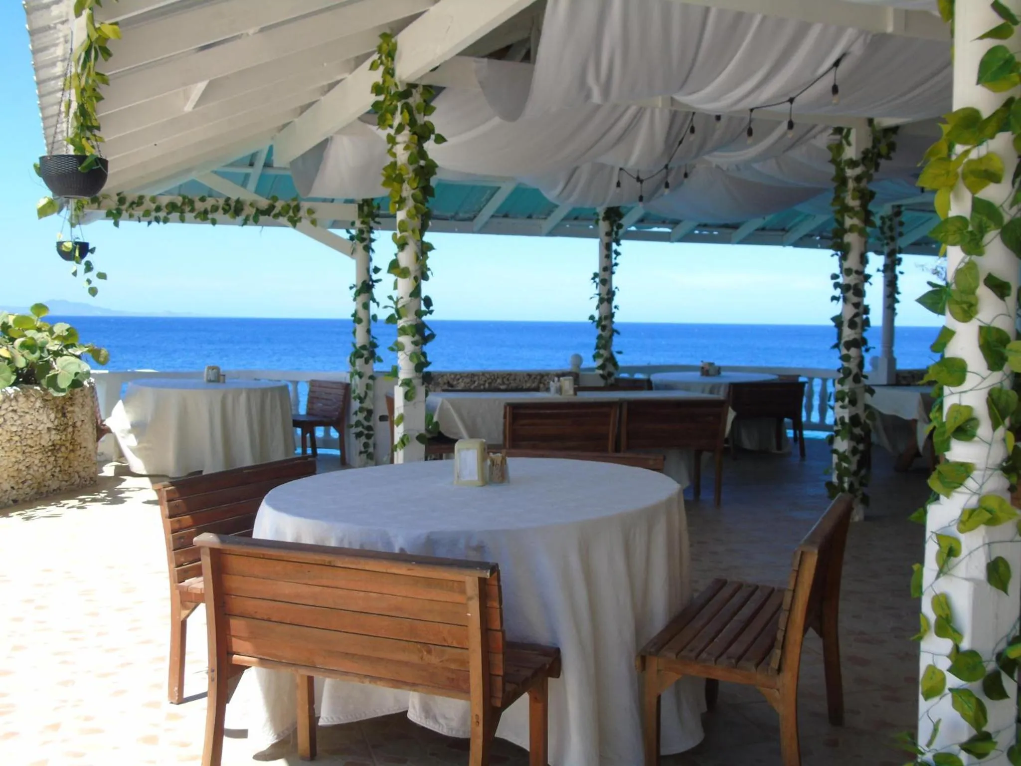 Terrasse ombragée avec tables et chaises donnant sur la mer.
