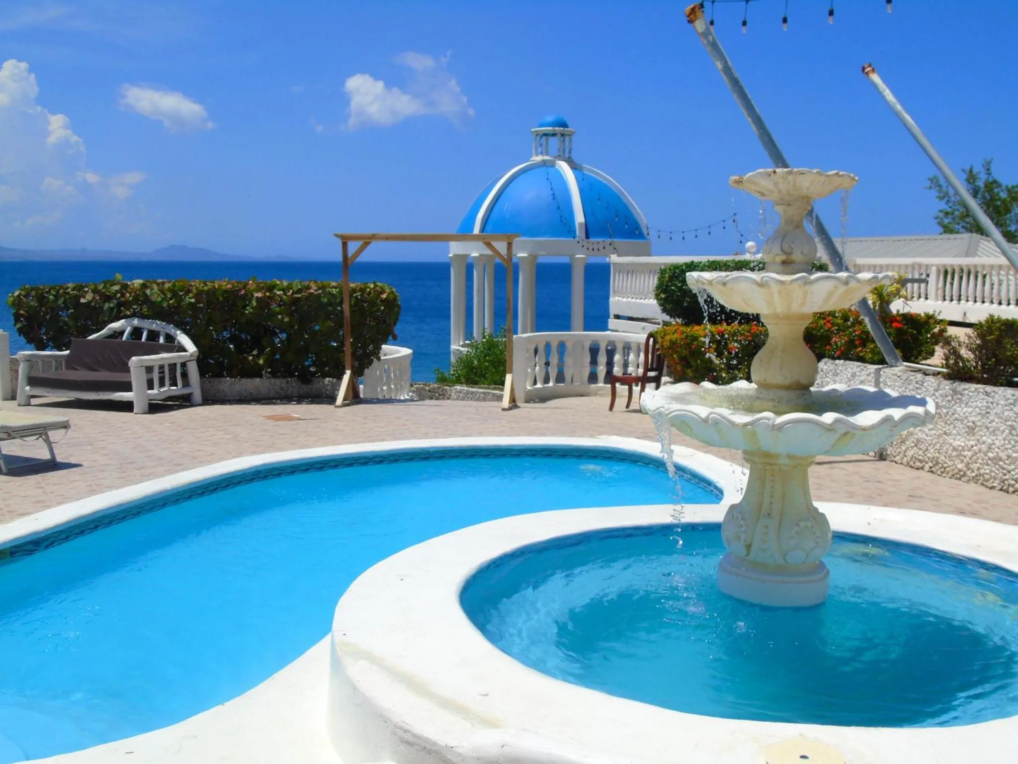 Une fontaine orne une terrasse avec piscine et vue sur la mer.