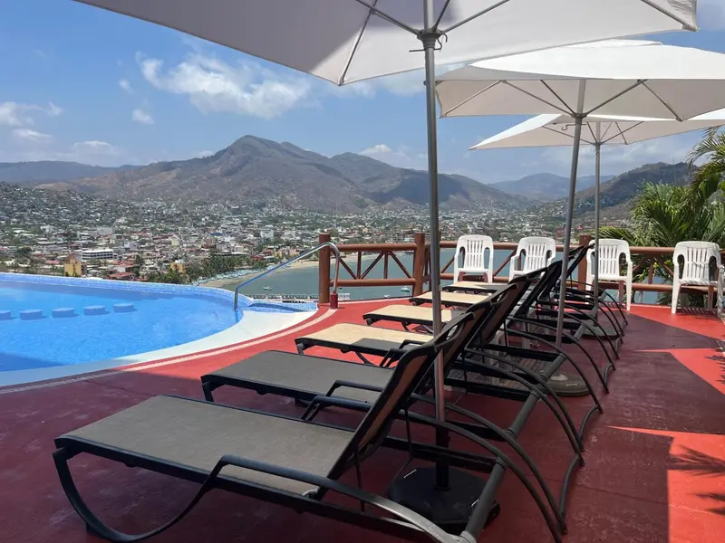 Transats et parasols bordent une piscine à débordement avec vue sur la ville et les montagnes.