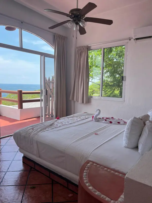 Une chambre lumineuse avec un lit décoré de fleurs et une vue sur la mer.