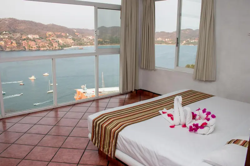 Chambre avec un grand lit et une vue sur la mer à travers de larges baies vitrées.