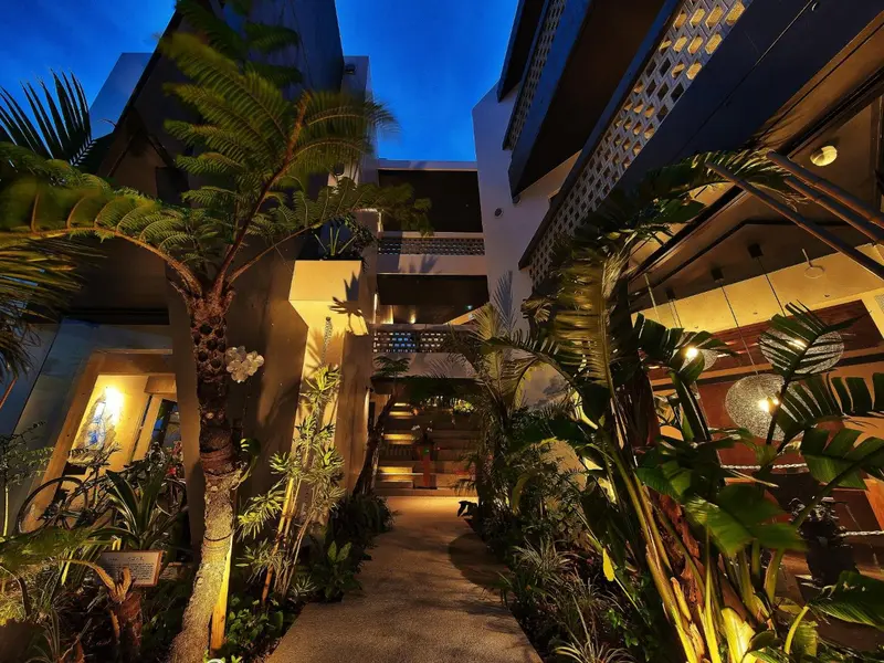 Allée illuminée dans une cour intérieure tropicale avec végétation luxuriante.